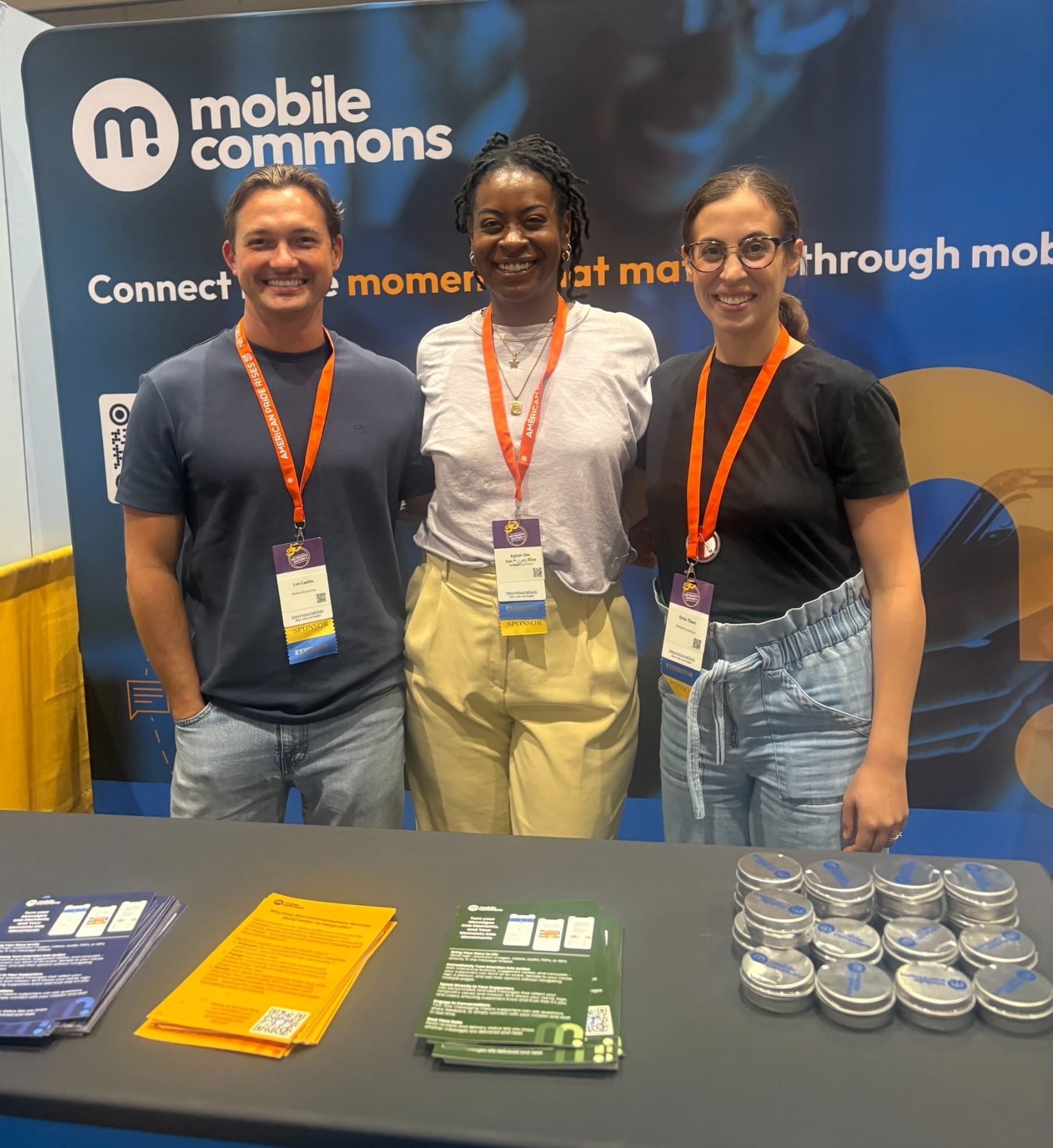 2025 Netroots 002 Three Mobile Commons staffers standing behind a branded event booth
